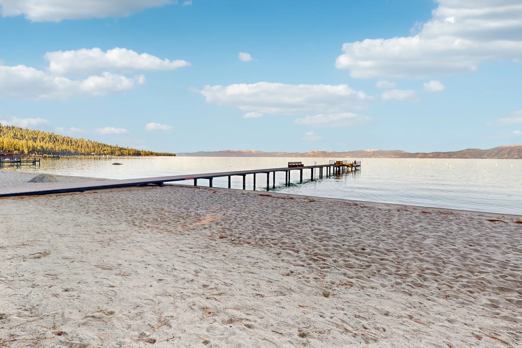 Zona común: Una orilla arenosa con un largo muelle que se extiende sobre aguas tranquilas.