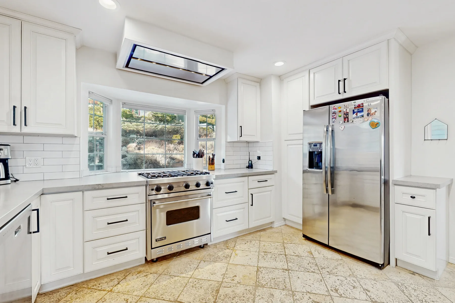 Una cocina blanca y luminosa con una estufa central y un refrigerador de acero inoxidable.