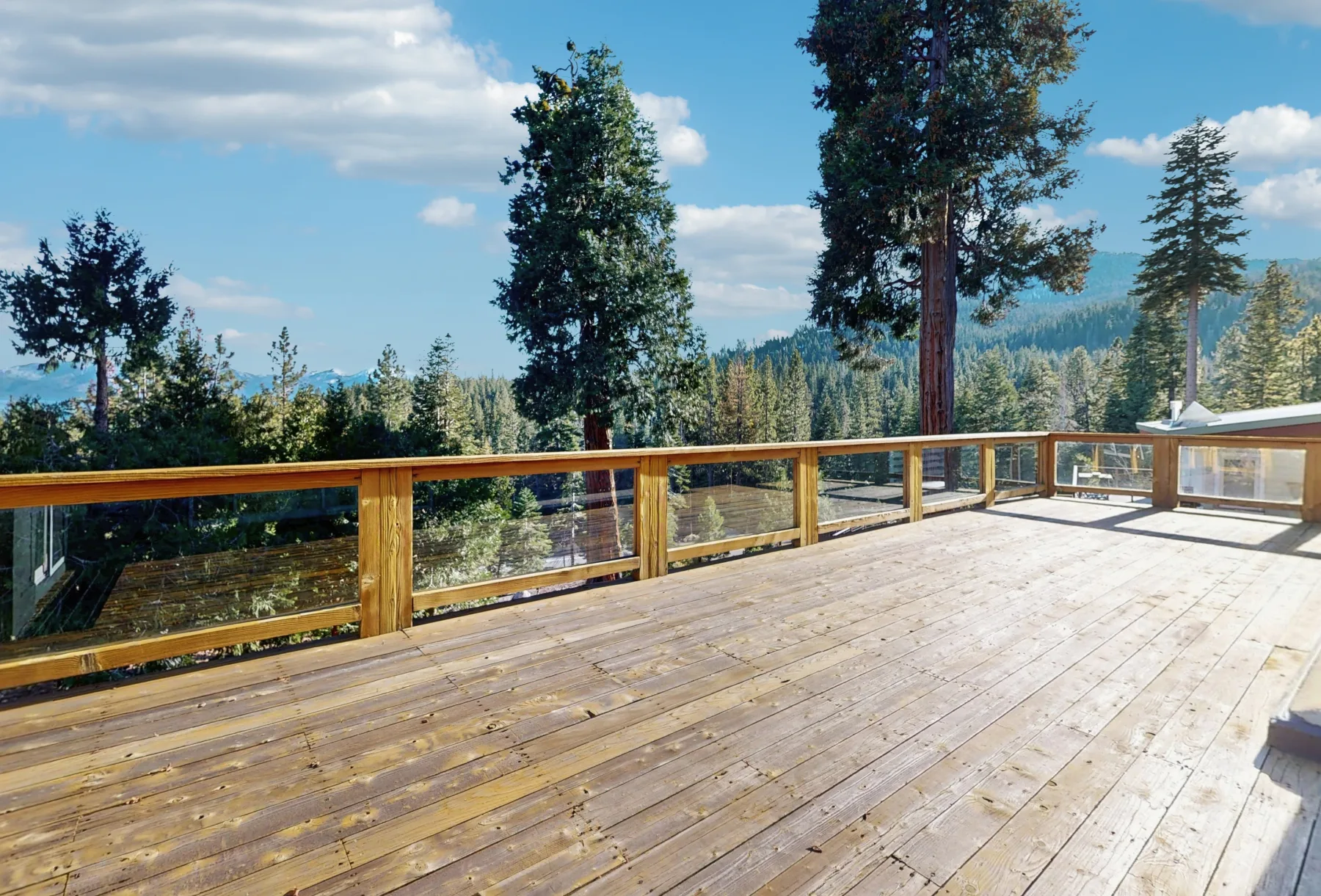 Una terraza de madera con barandilla de vidrio da a un paisaje boscoso.