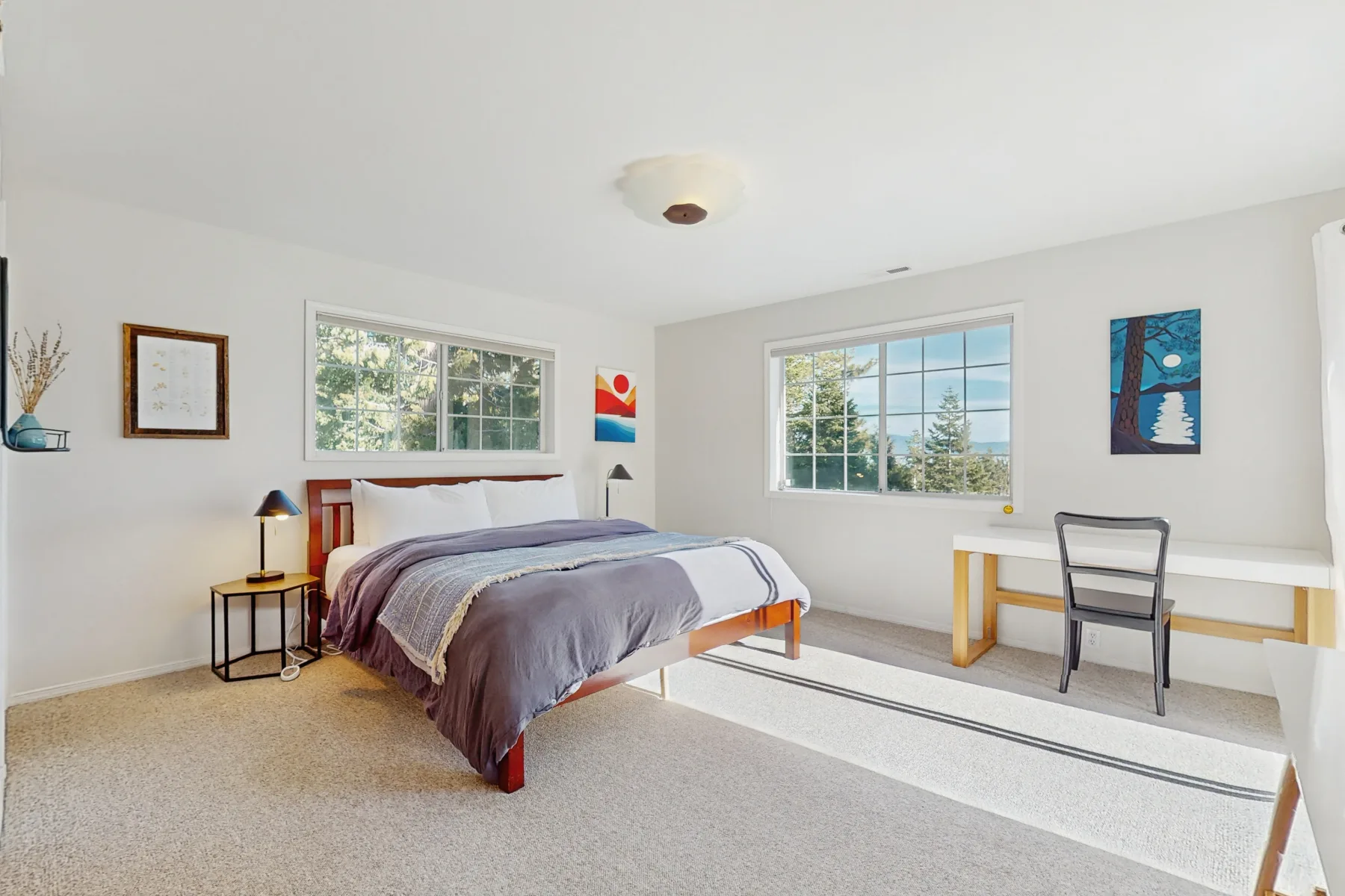Un dormitorio luminoso con una cama y un escritorio junto a grandes ventanas.
