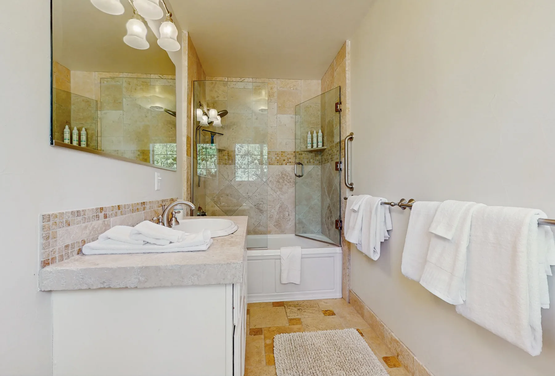 Un baño luminoso tiene un lavabo junto a una ducha de vidrio y una bañera.