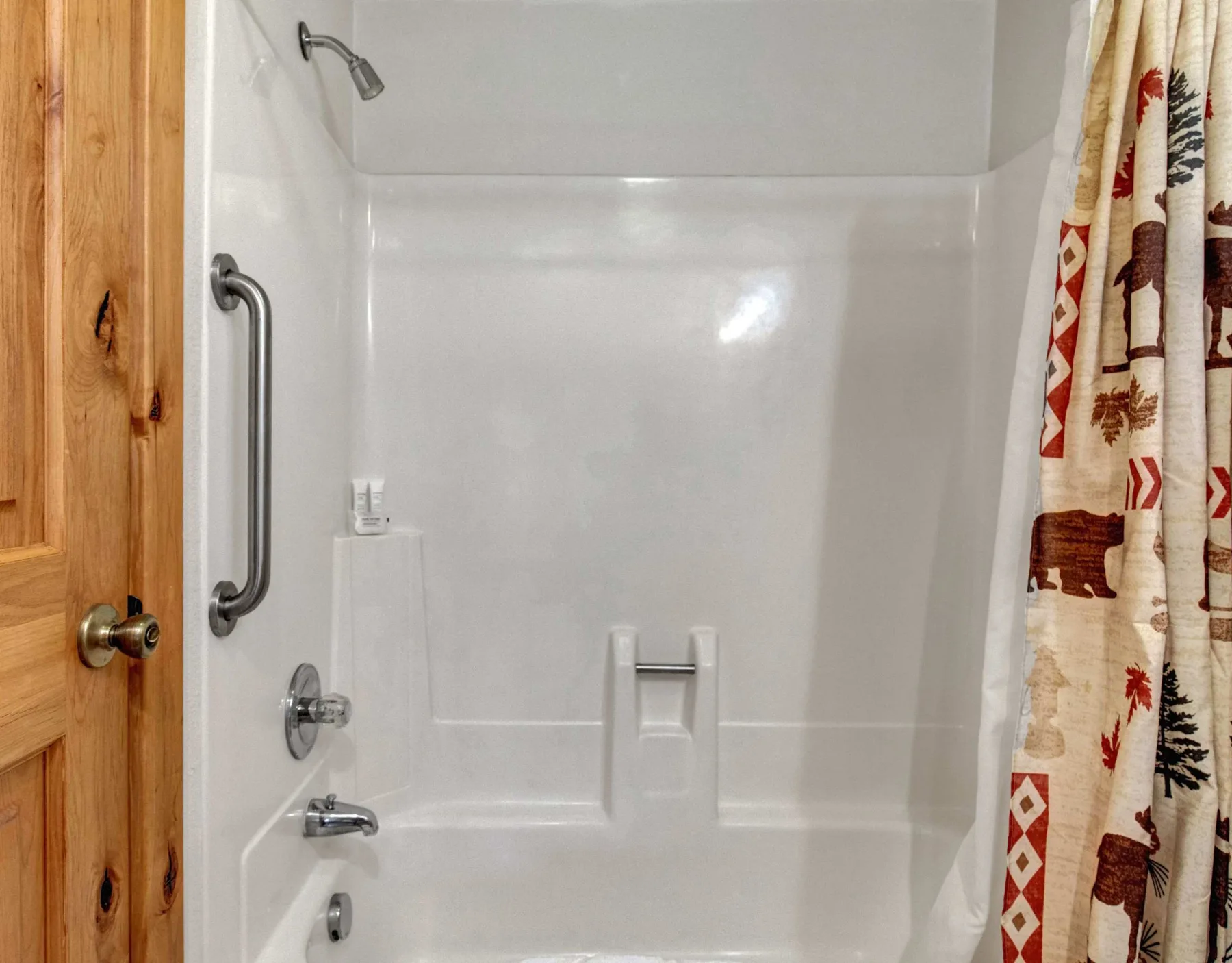 Un baño con ducha, cortina estampada y puerta de madera.