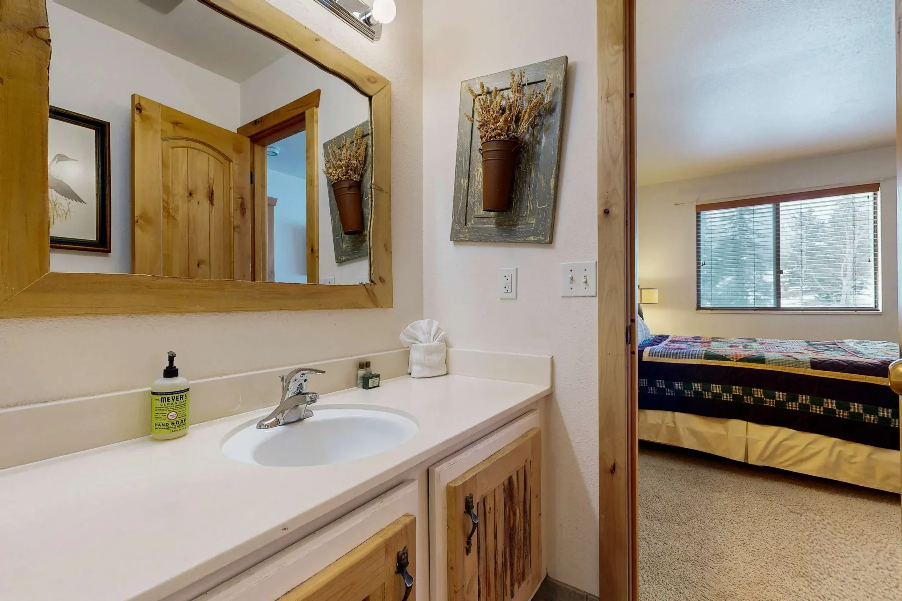 Un lavabo de baño da a un dormitorio a través de una puerta abierta.