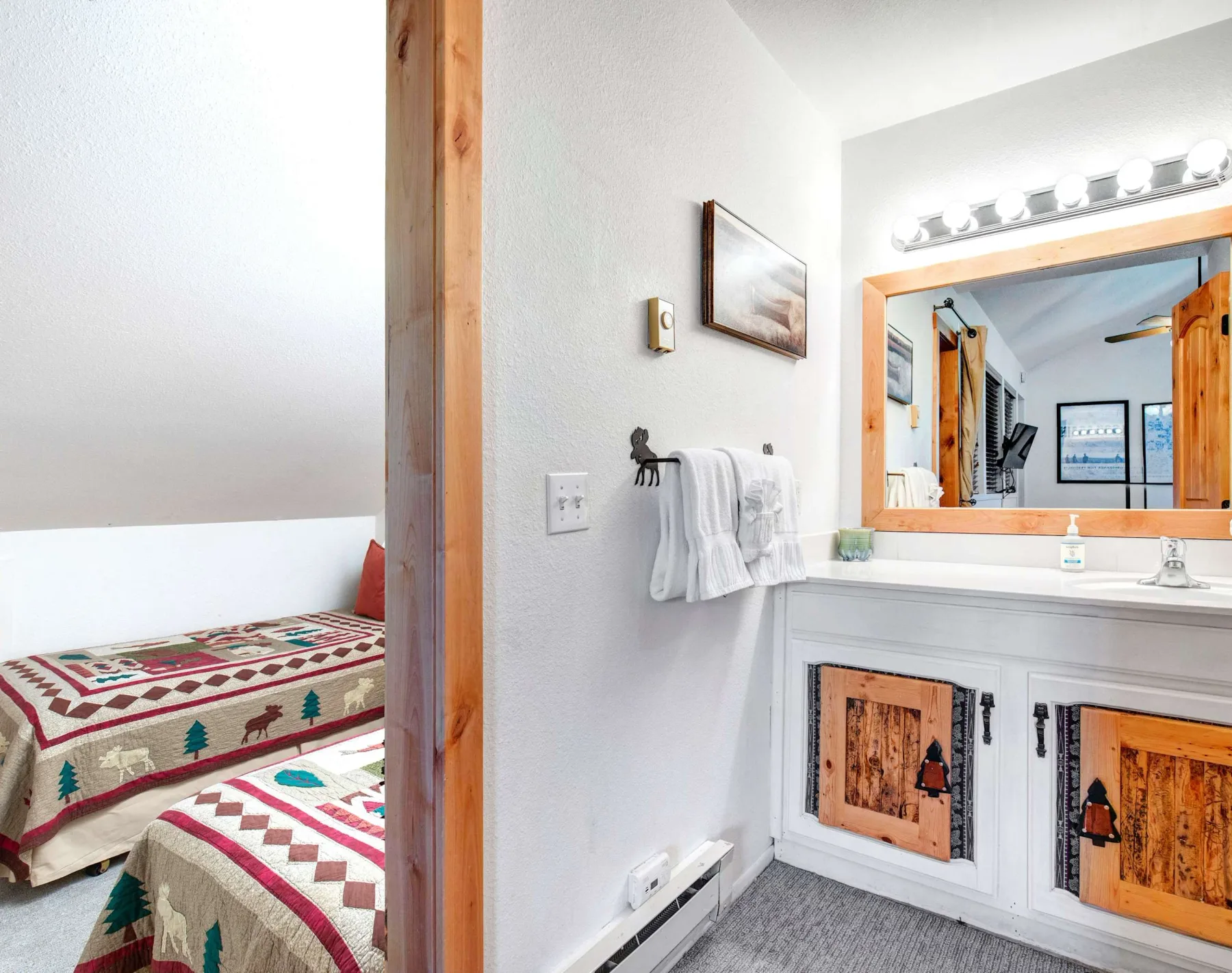 Un tocador de baño con espejo junto a una zona para dormir con ropa de cama estampada.