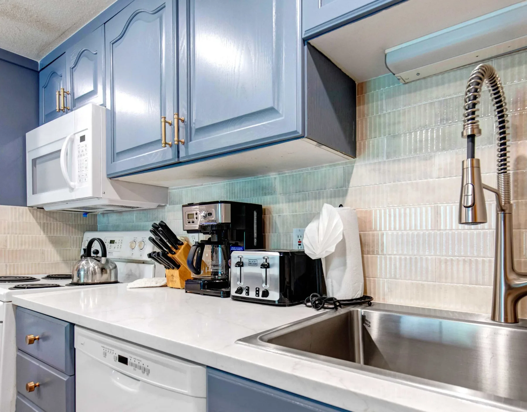 Una cocina con gabinetes azules, una encimera blanca y un fregadero de acero inoxidable.