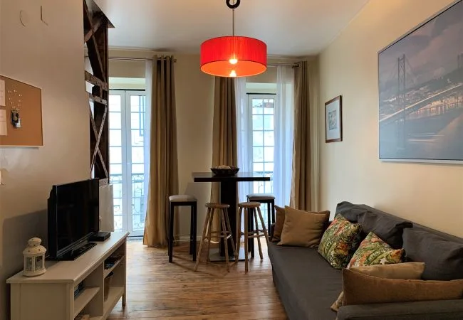 A living room with a dining table beside tall windows and a sofa.