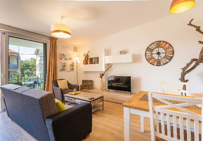 Una luminosa sala de estar y comedor con asientos, un televisor y una mesa junto a la ventana.