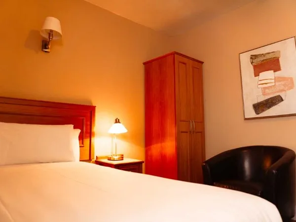 Espacio representativo del hotel: Un dormitorio con luz cálida, una cama, un armario de madera y un asiento oscuro.