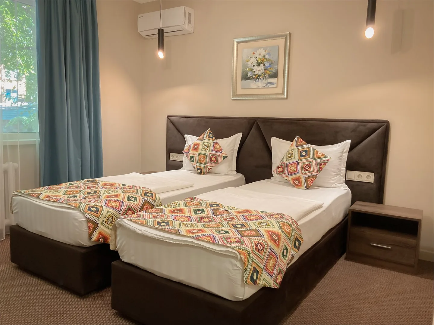 Espacio representativo del hotel: Un dormitorio con dos camas vestidas con sábanas blancas y cubrecamas estampados de colores.