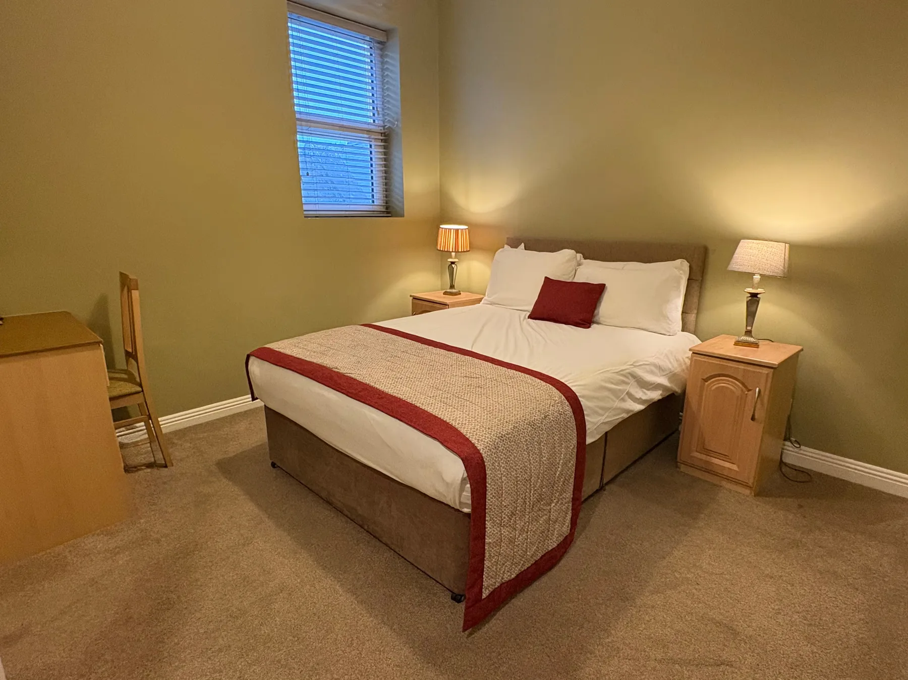 Espacio representativo del hotel: Un dormitorio con una cama, un cojín rojo y lámparas de noche.