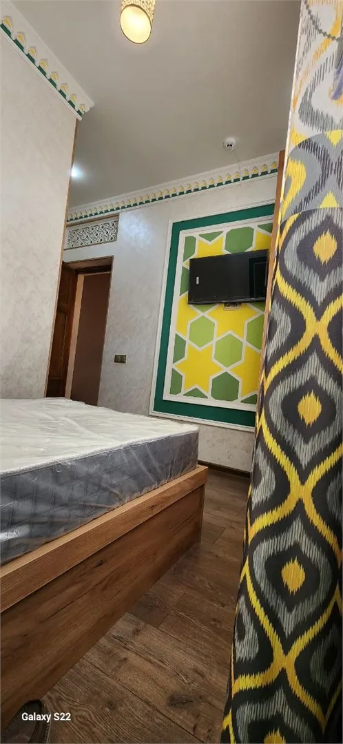 Espacio representativo del hotel: Un dormitorio con cama, televisor en la pared y cortina estampada.