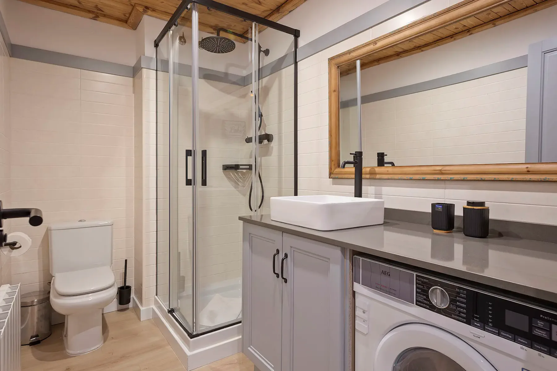 A modern bathroom with a glass shower and a vanity beside a washing machine.