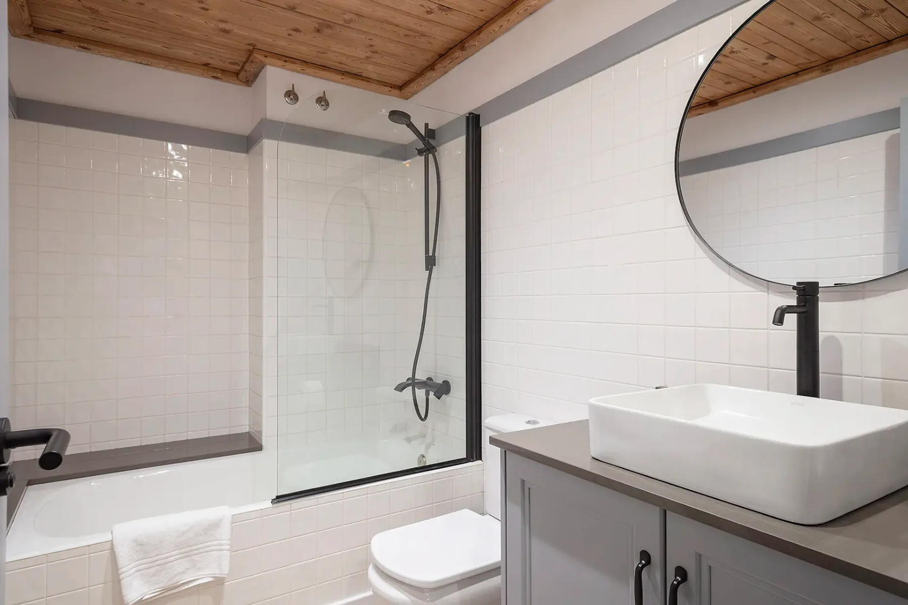 A tiled bathroom with a shower, sink, and round mirror.