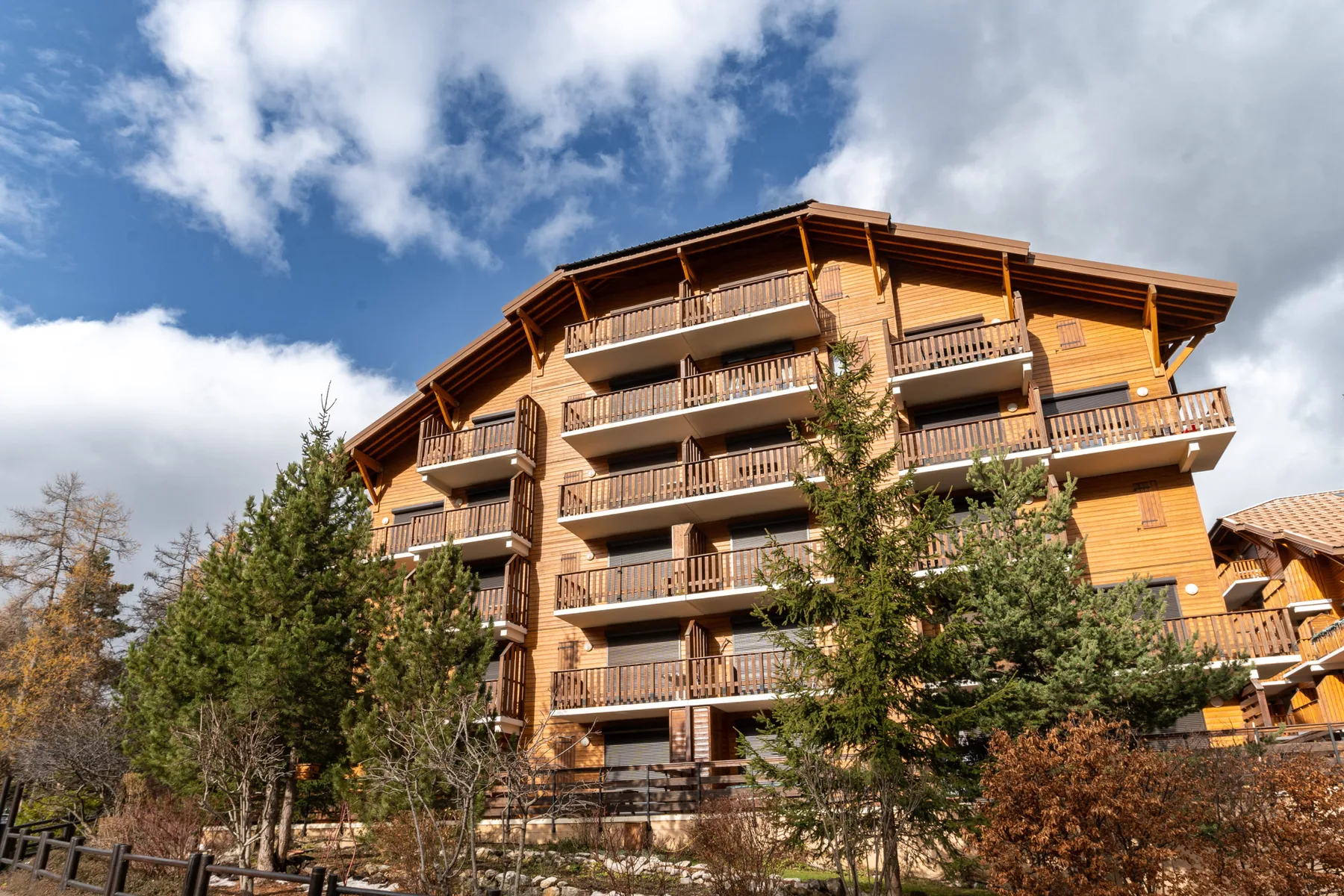 Shared amenity: A multi-story wooden building with balconies stands among trees under a partly cloudy sky.
