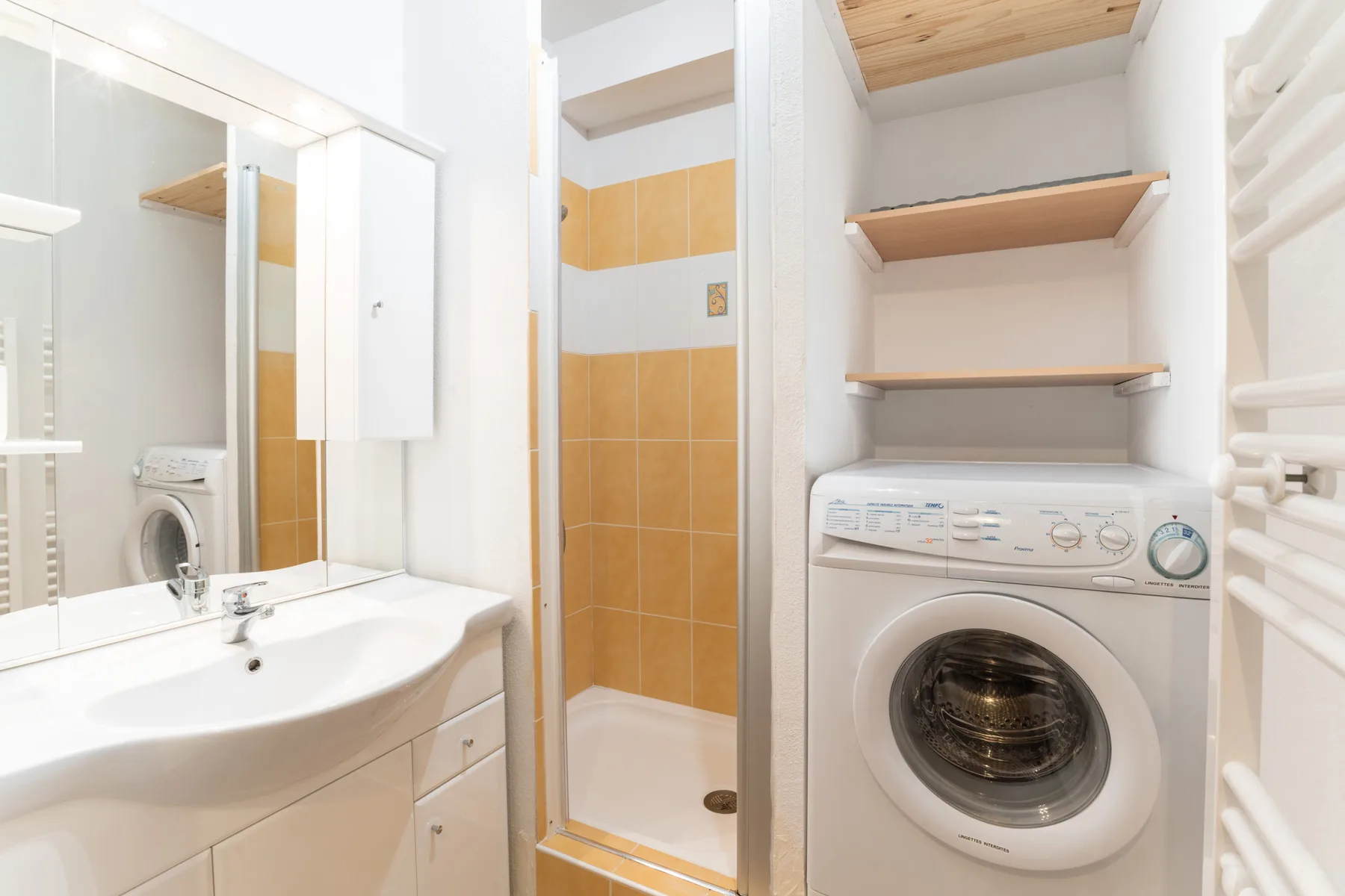 A bathroom with a sink, shower, and front-loading washing machine.