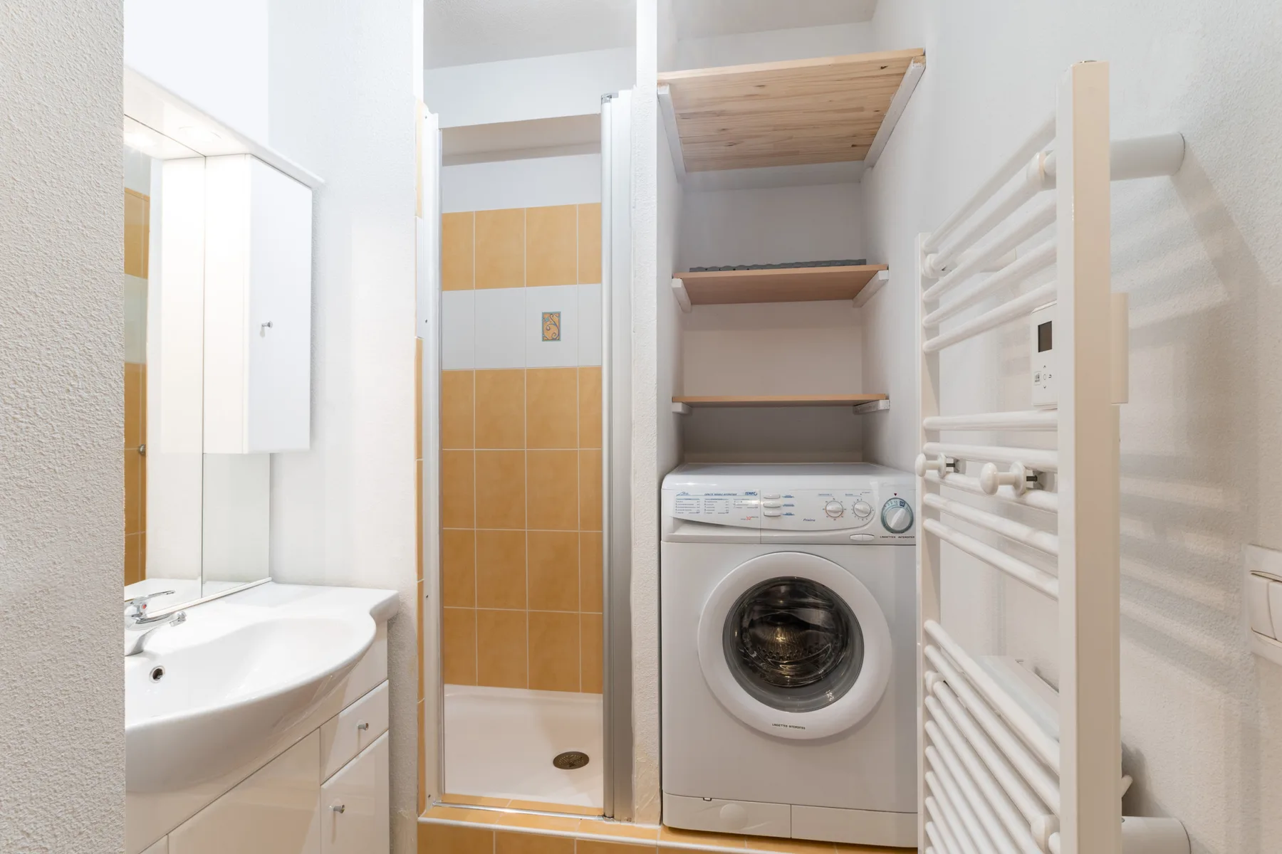 A bathroom with a washing machine, sink, and tiled shower.