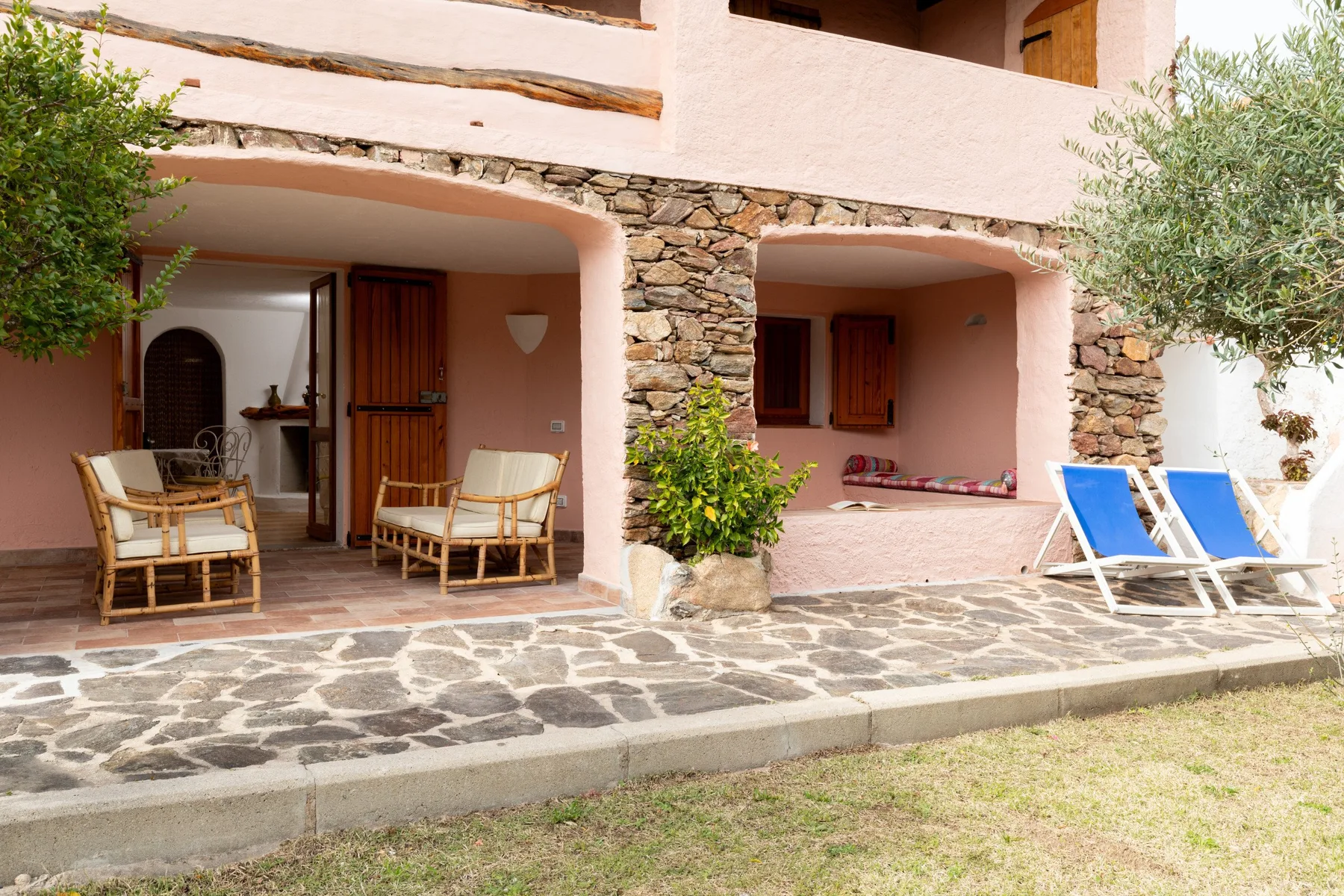 A shaded patio with seating, blue loungers, and a stone-paved terrace.