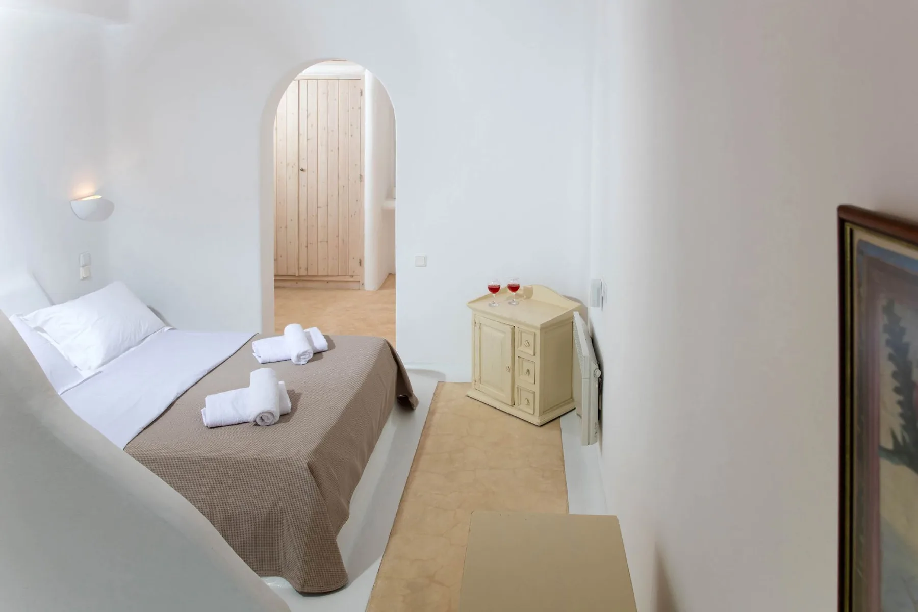 A bright bedroom with a bed, folded towels, and an arched doorway.