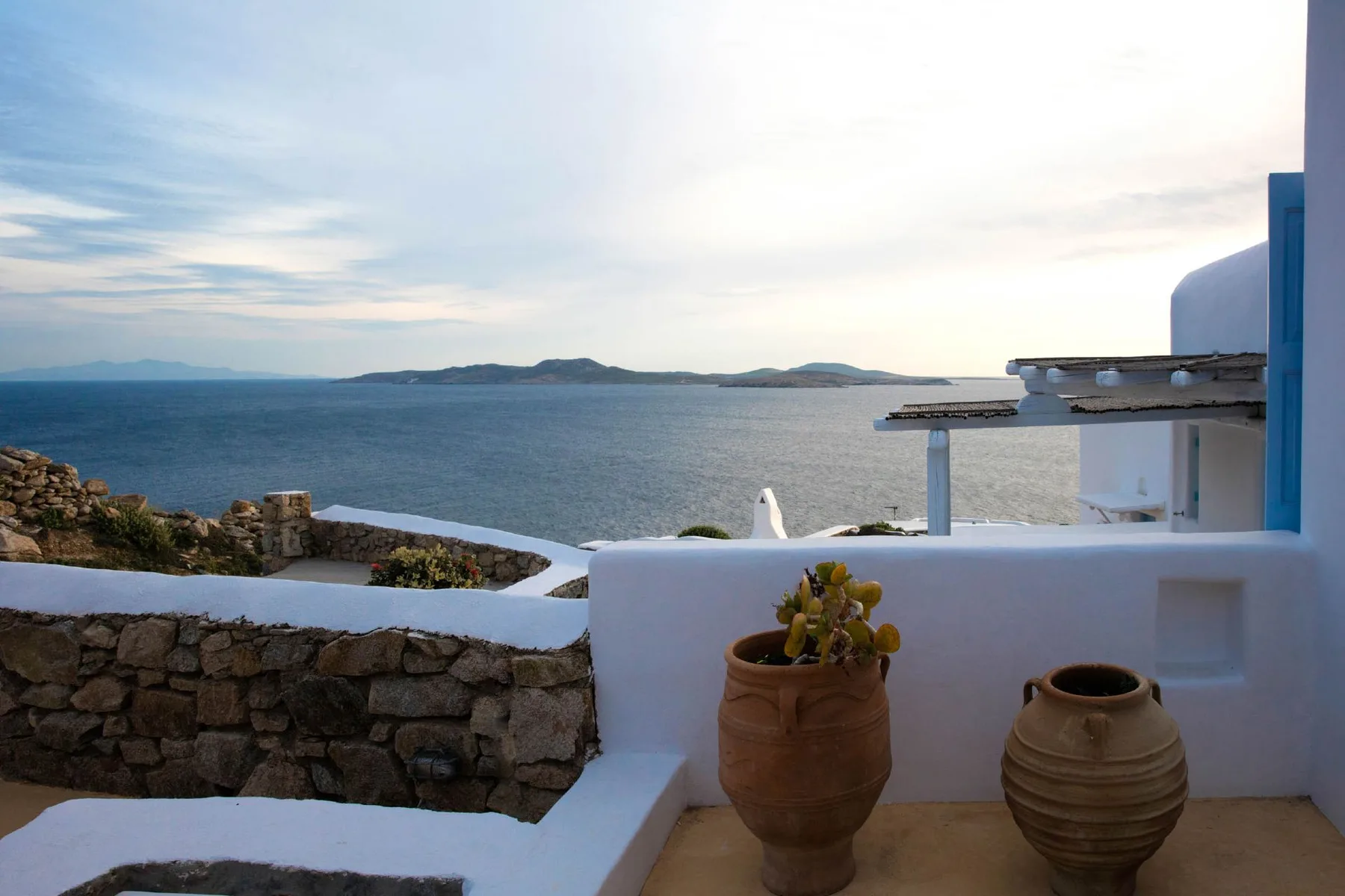 A seaside terrace overlooks calm water and distant islands, with potted plants in the foreground.
