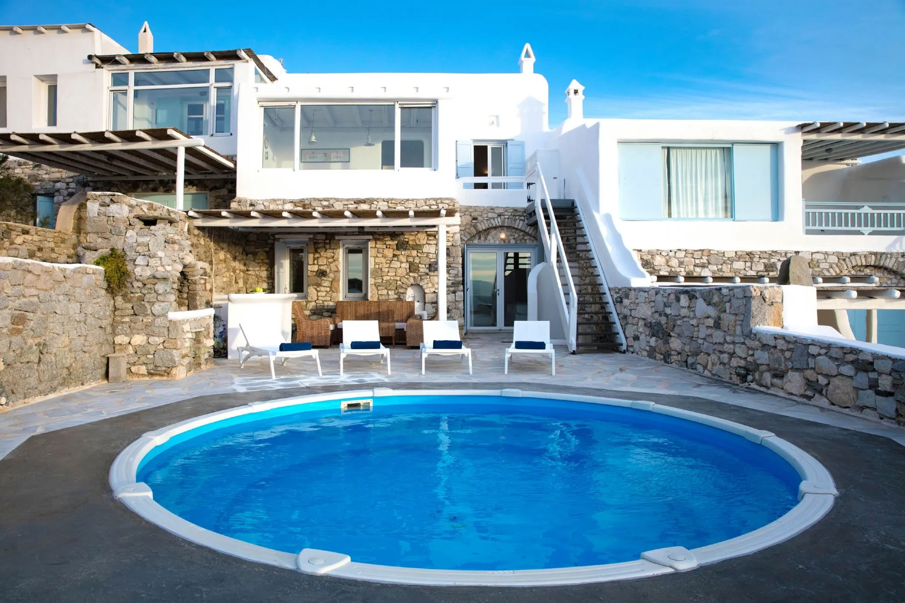 A blue swimming pool sits in front of a white building with stone walls.