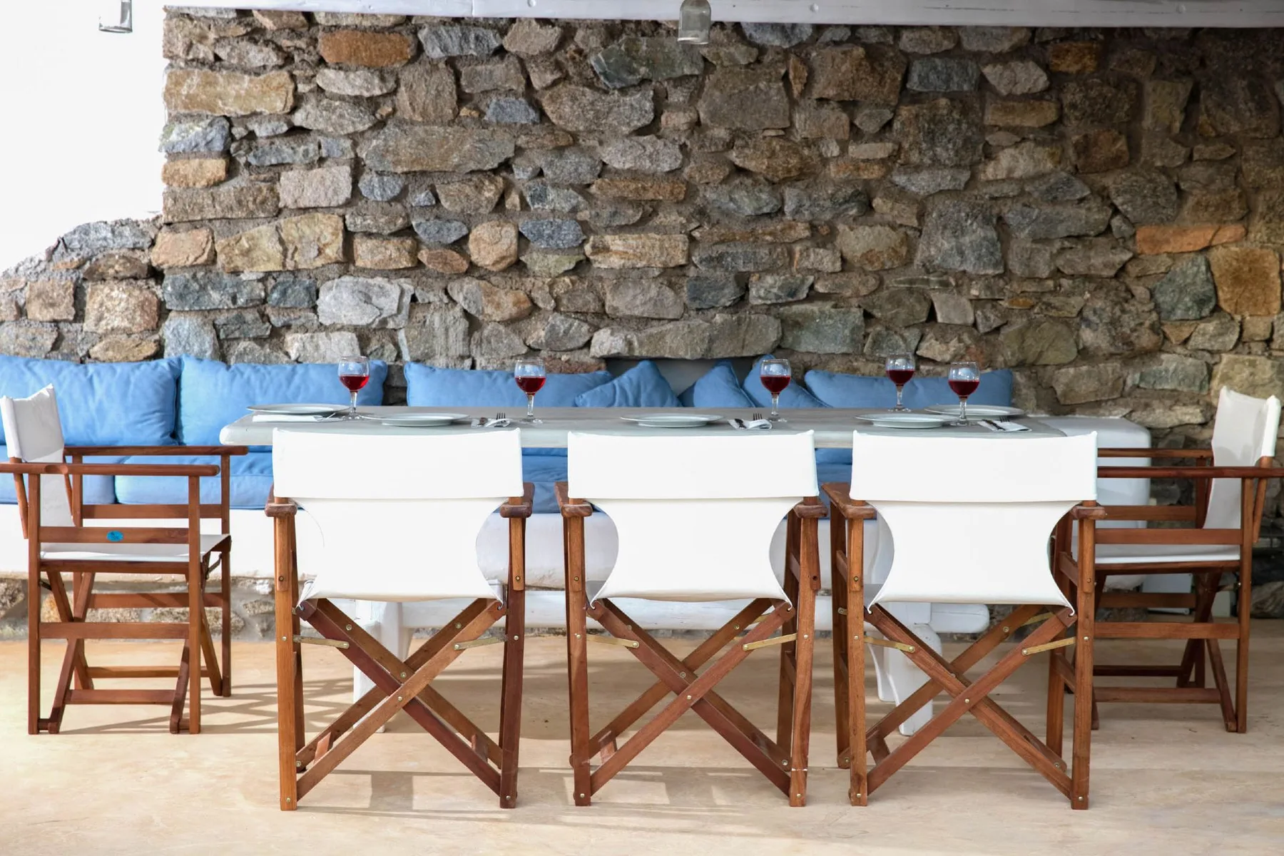 An outdoor dining area has a long table surrounded by wooden and white seating.