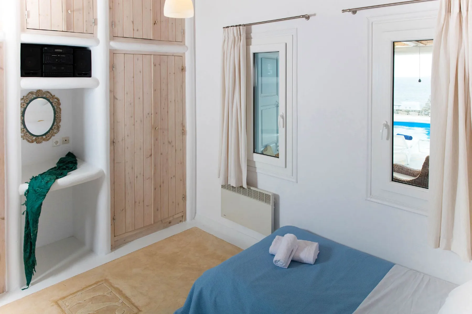 A bedroom with a blue-covered bed, built-in shelves, and two windows.