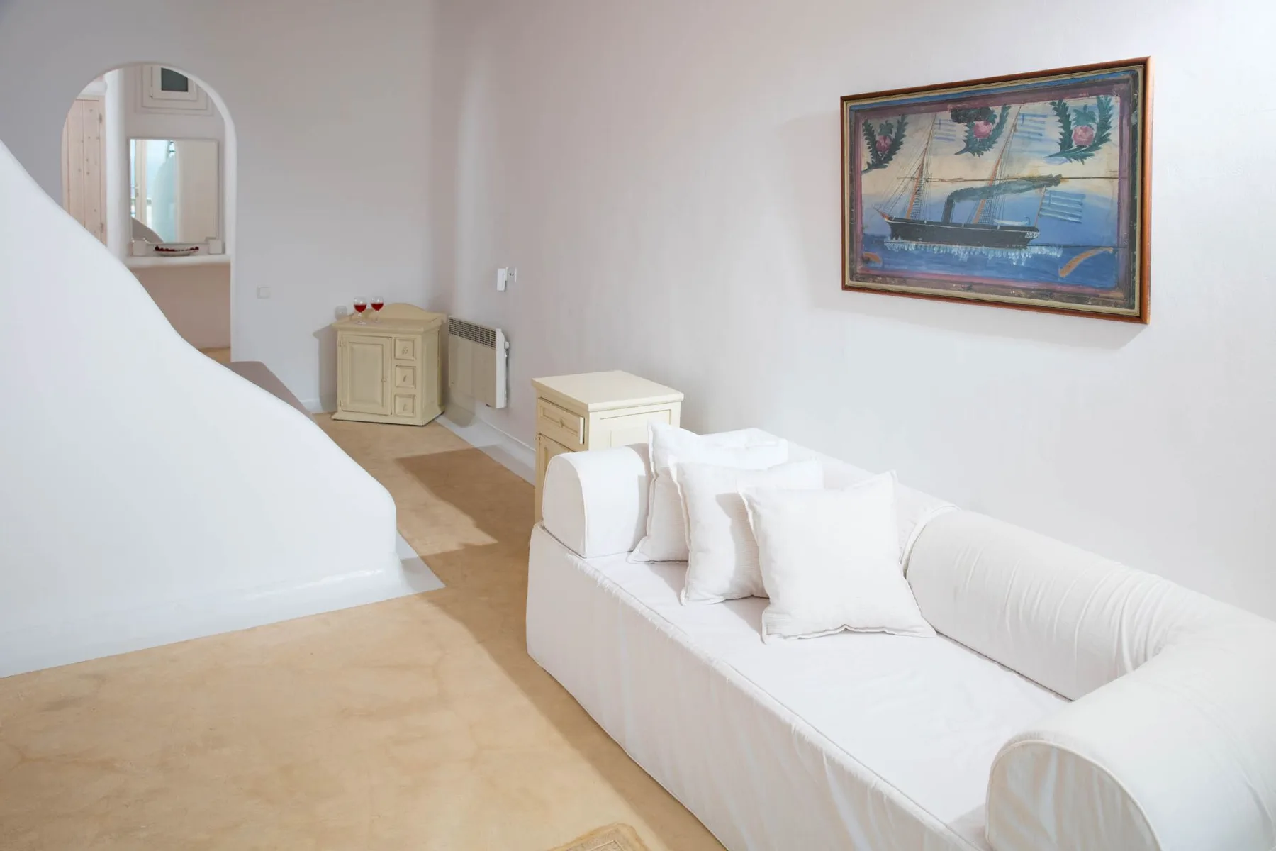 A bright sitting room with white seating and framed artwork on the wall.