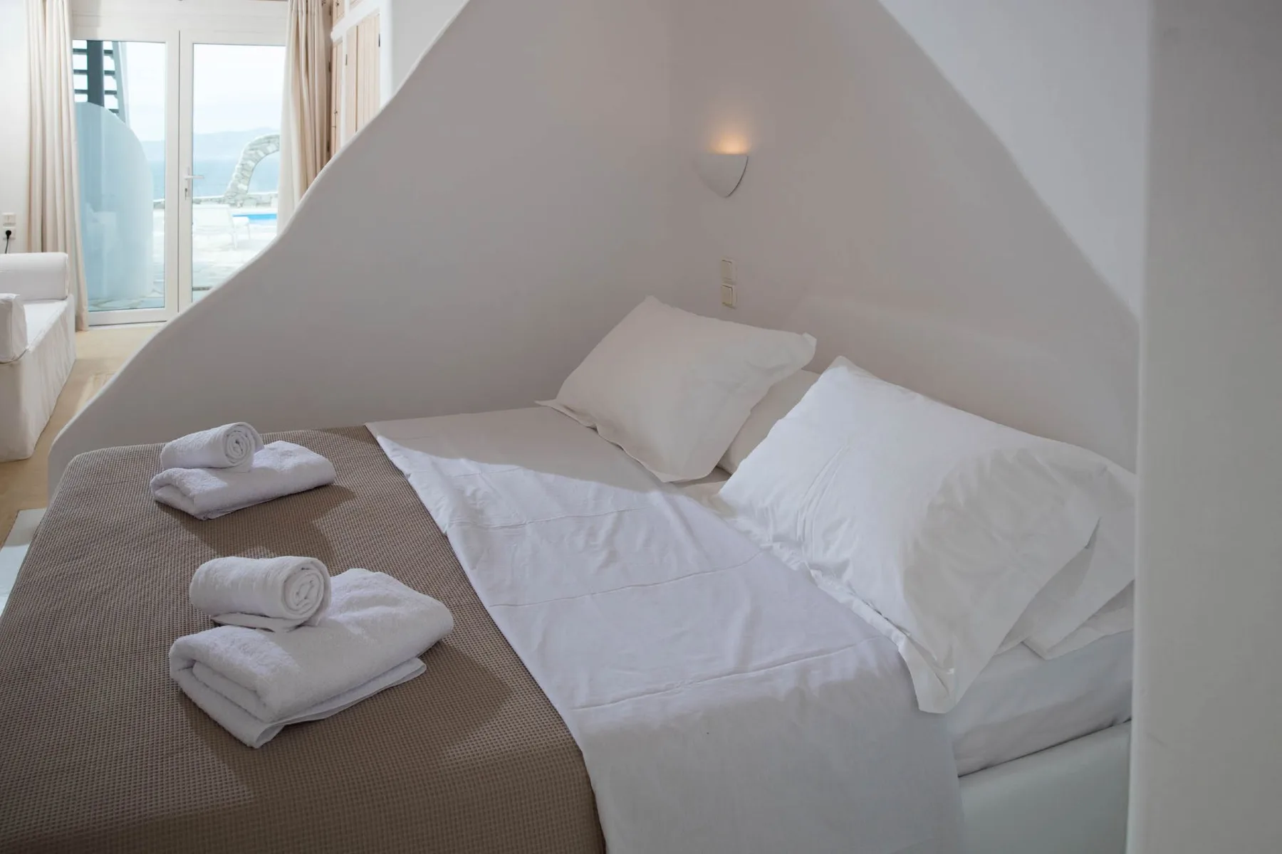 A bedroom with a bed, white bedding, and folded towels.