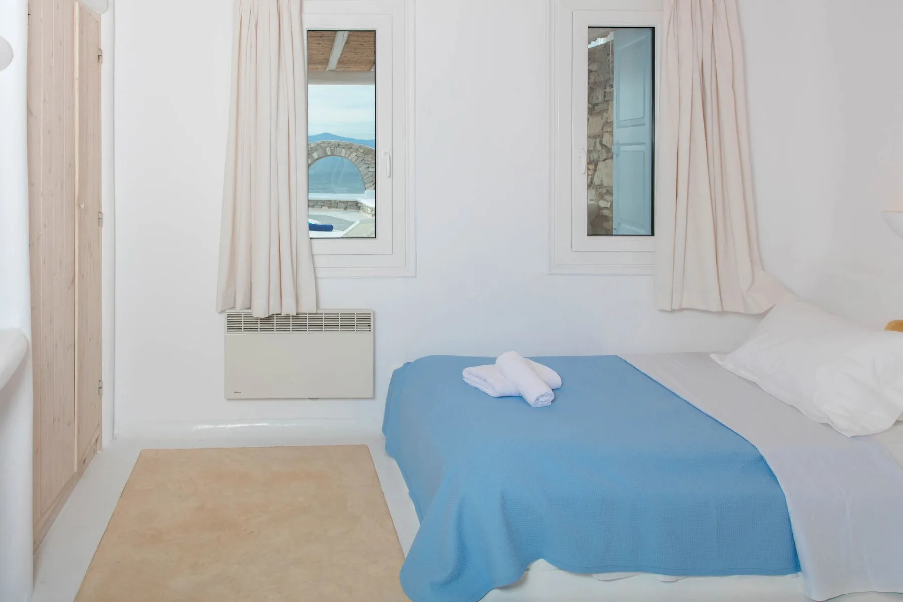 A bright bedroom with a blue bedspread and two narrow windows.