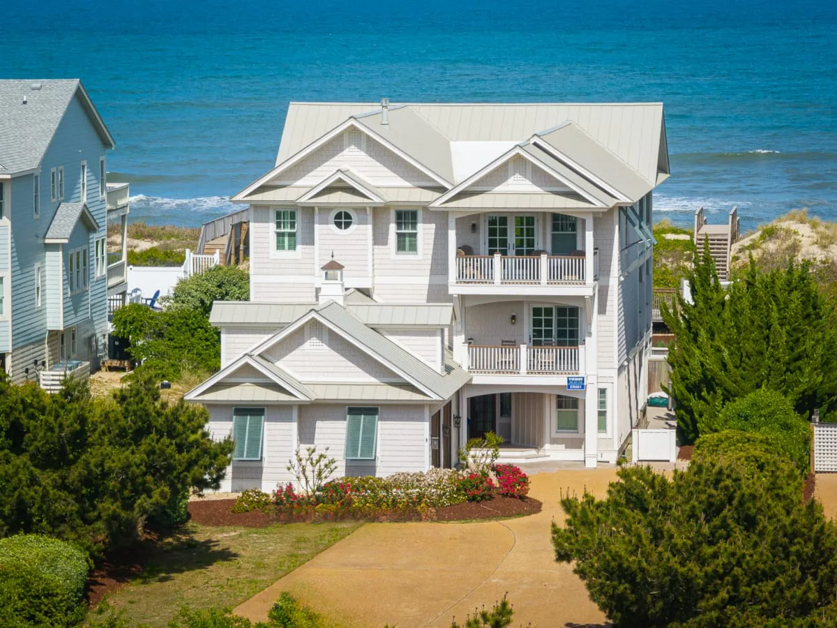 Una gran casa costera está junto a la playa, con el océano visible detrás.