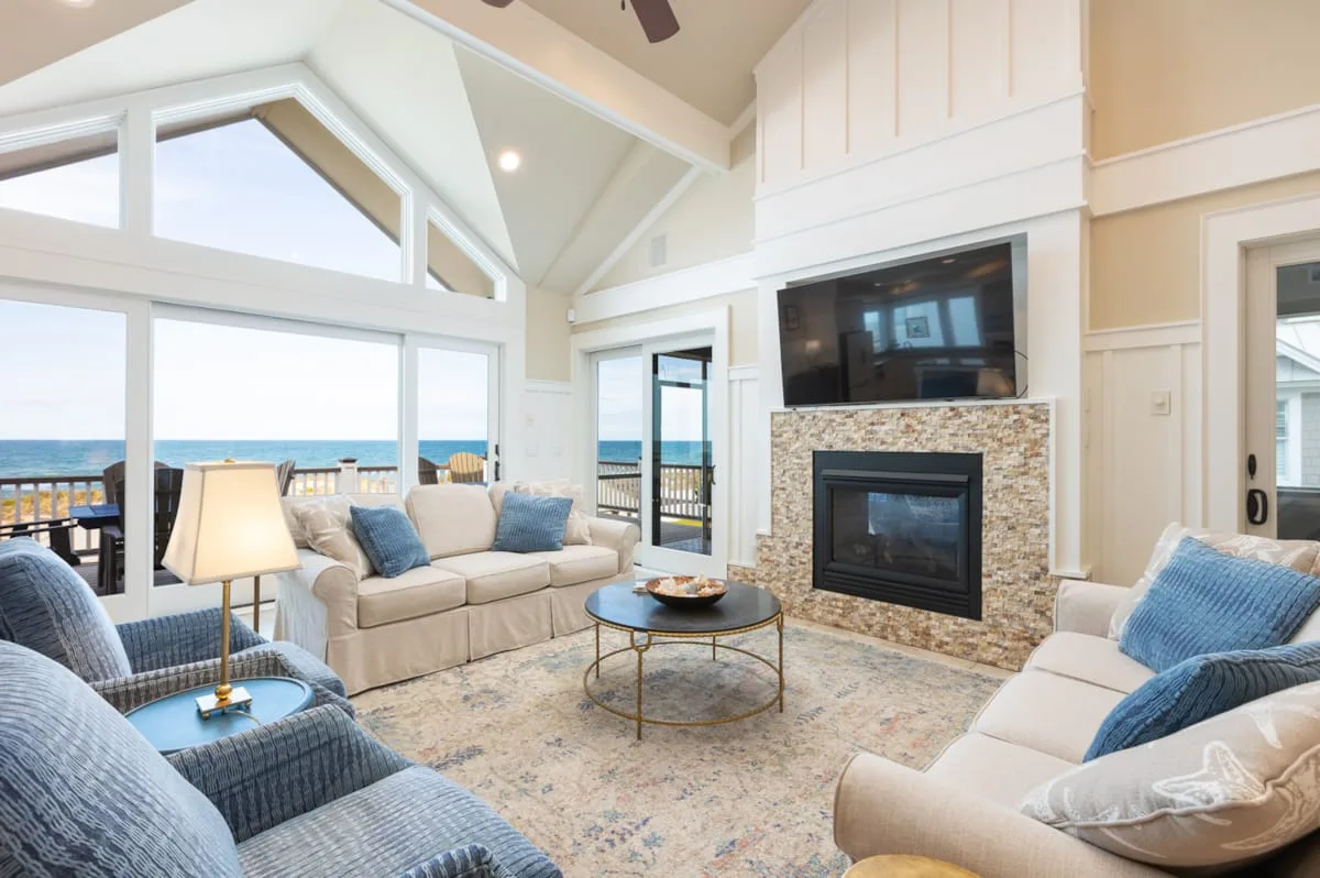 Una sala luminosa con asientos, una chimenea y grandes ventanas con vistas al agua.