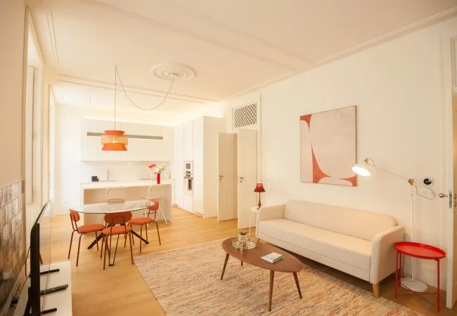 Una luminosa sala-comedor diáfana con sofá, mesa y cocina.