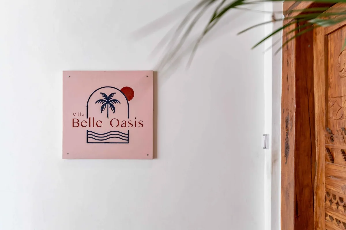 A white entryway wall displays a pink sign beside a carved wooden door.