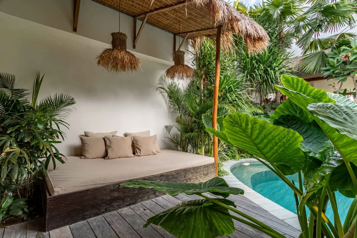 A tropical outdoor lounge with cushioned seating beside a small pool.