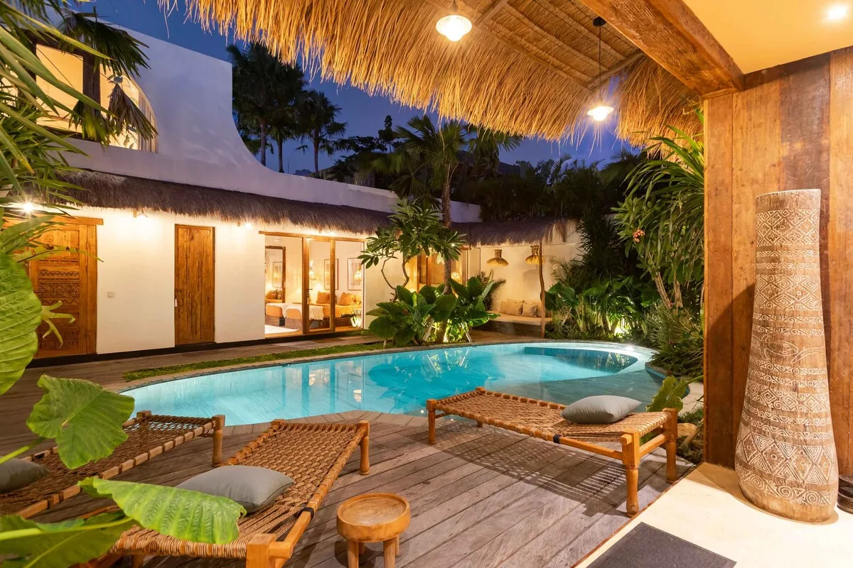 A tropical courtyard features a swimming pool, wooden loungers, and lush plants.