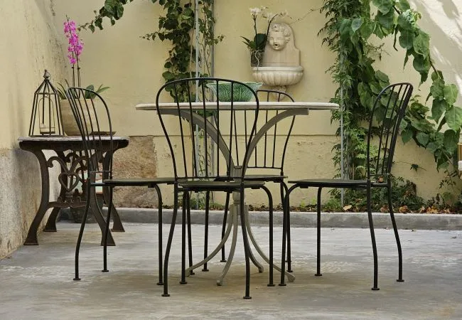 Una zona de estar al aire libre con mesa y sillas metálicas junto a una pared cubierta de enredaderas.