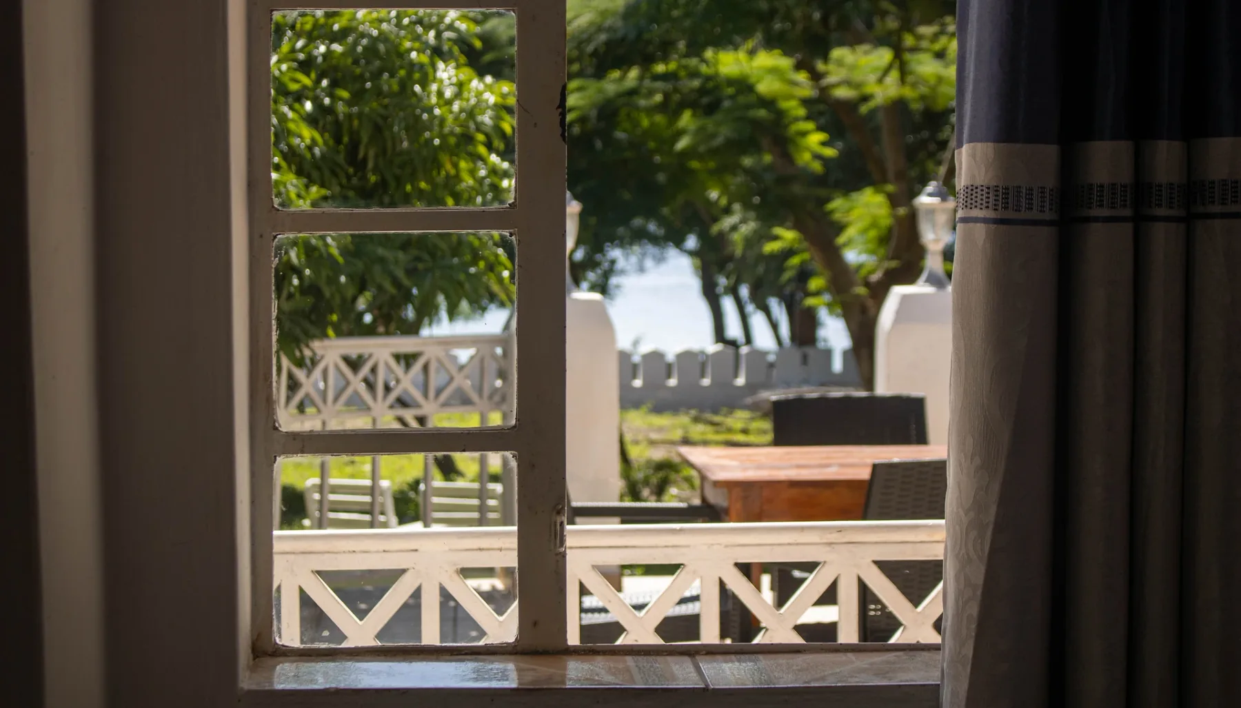 Espacio representativo del hotel: Una ventana da a una terraza exterior soleada con árboles y una barandilla.