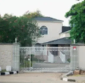 Espacio representativo del hotel: Una entrada exterior con portón y un edificio bajo entre árboles.