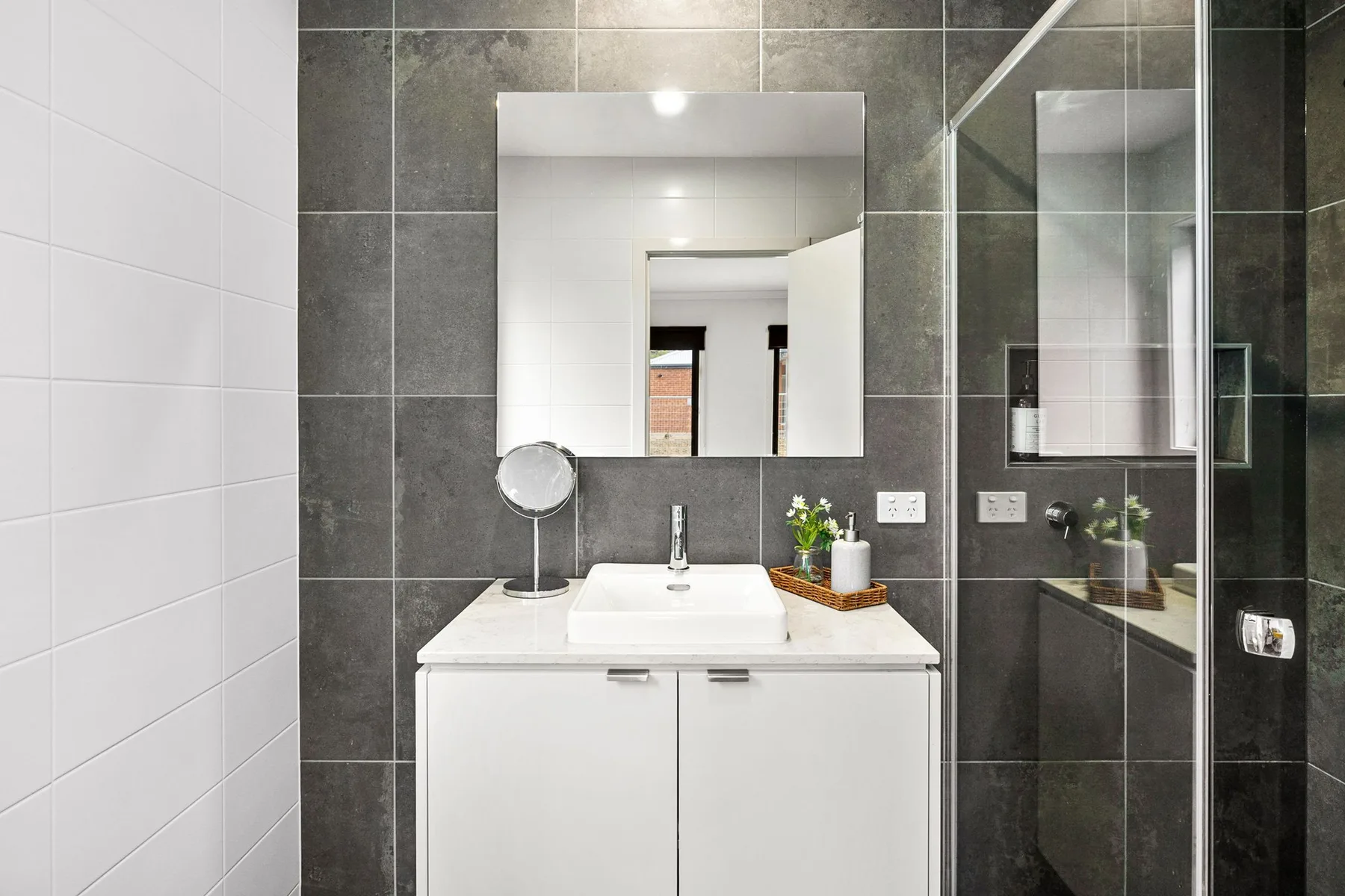 A bathroom vanity with a mirror stands beside a glass shower.