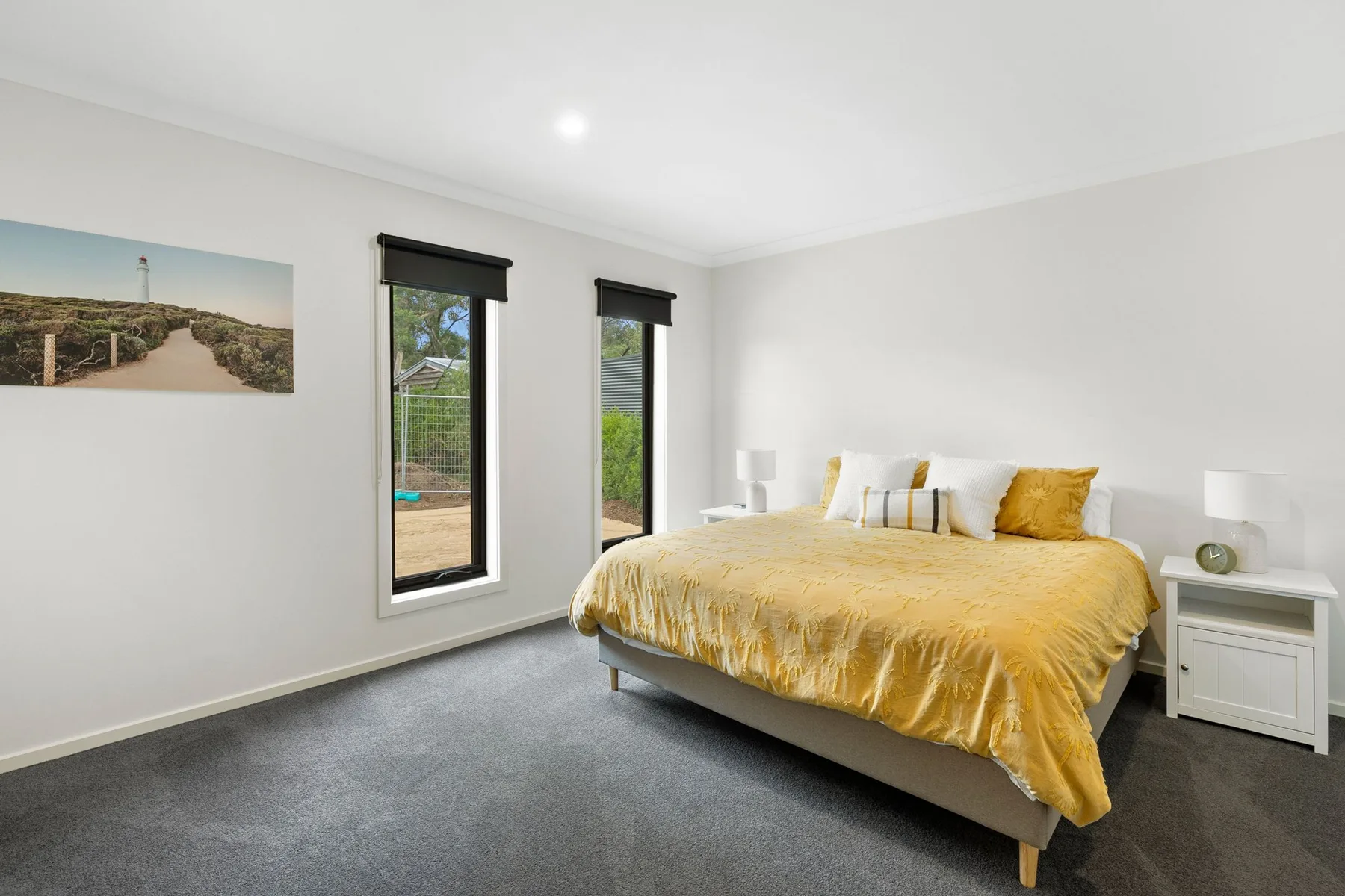 A bright bedroom with a bed dressed in golden bedding and tall windows.