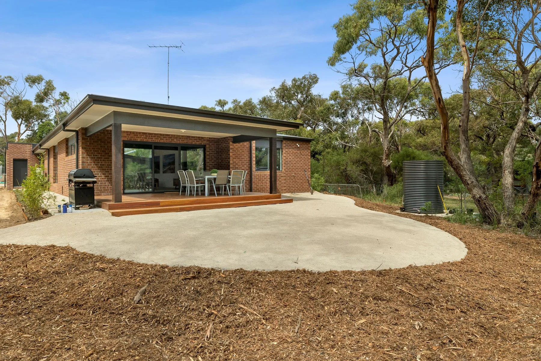 A brick house opens onto a broad paved patio with outdoor seating.