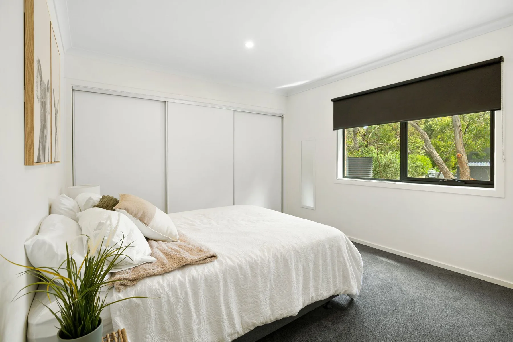 A bright bedroom with a bed beside a wide window overlooking greenery.