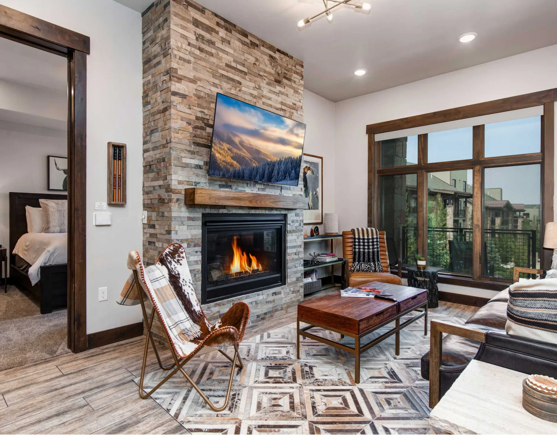 Una sala de estar con chimenea de piedra, televisor, asientos y ventanales.
