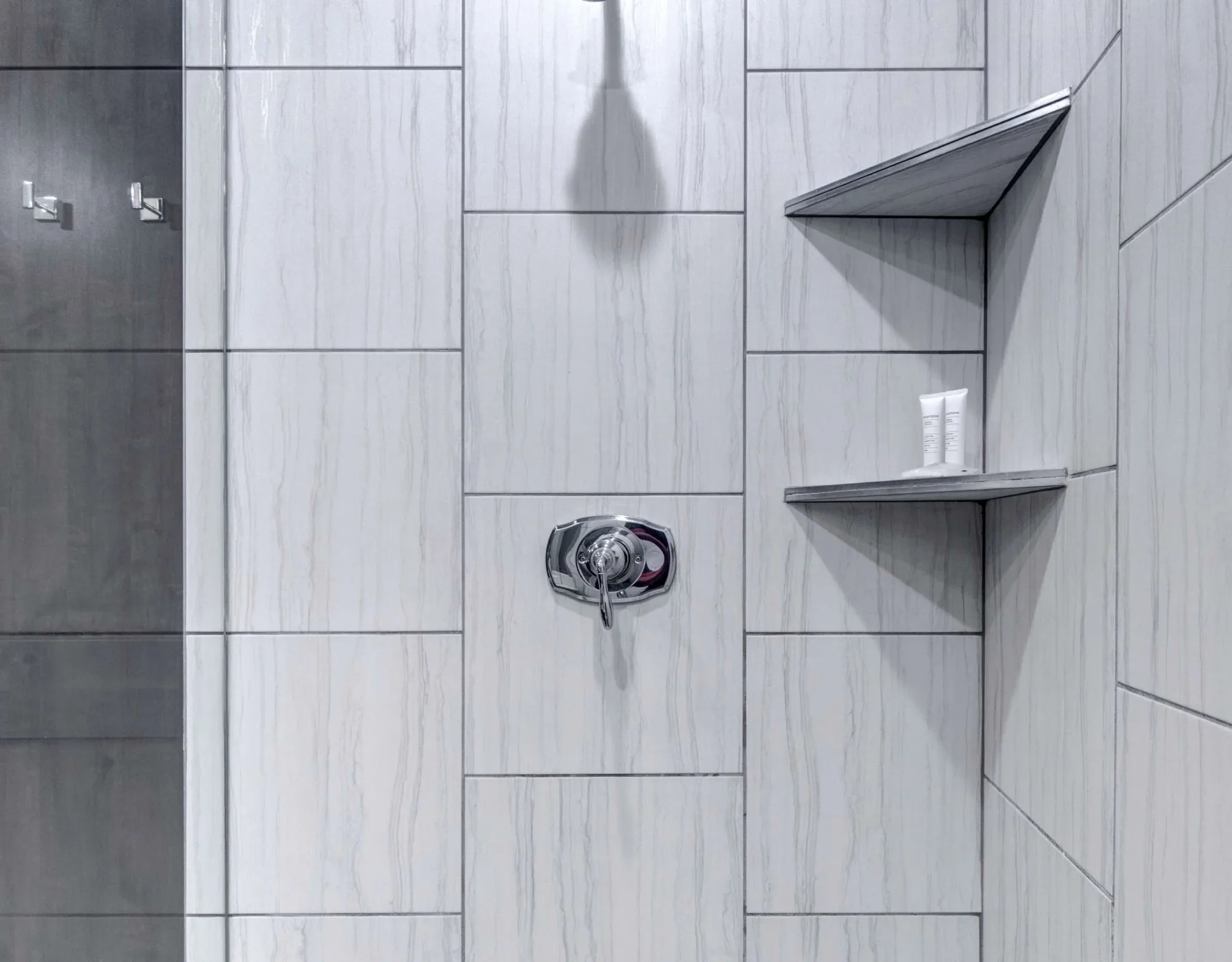 Una zona de ducha con azulejos, un control de pared y estantes en la esquina.