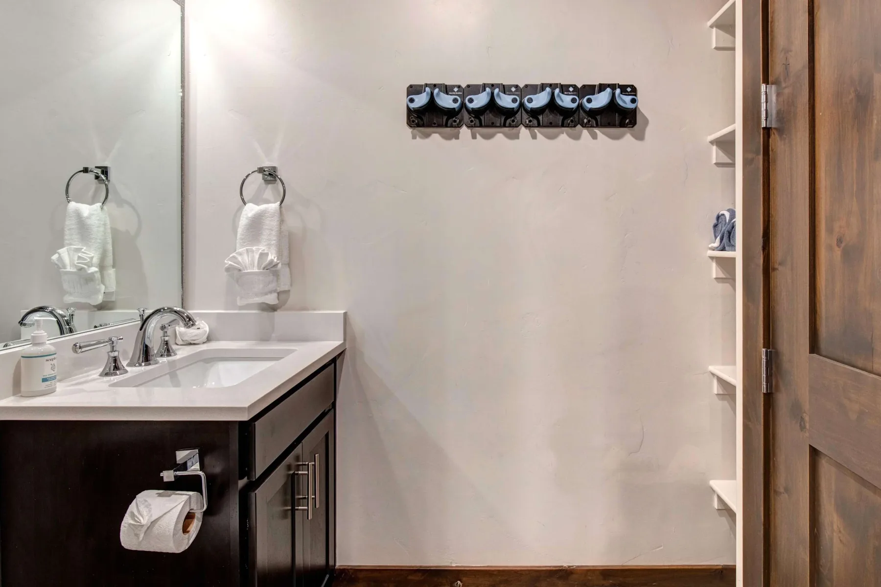 Un lavabo de baño está junto a una pared con ganchos y una puerta de madera.