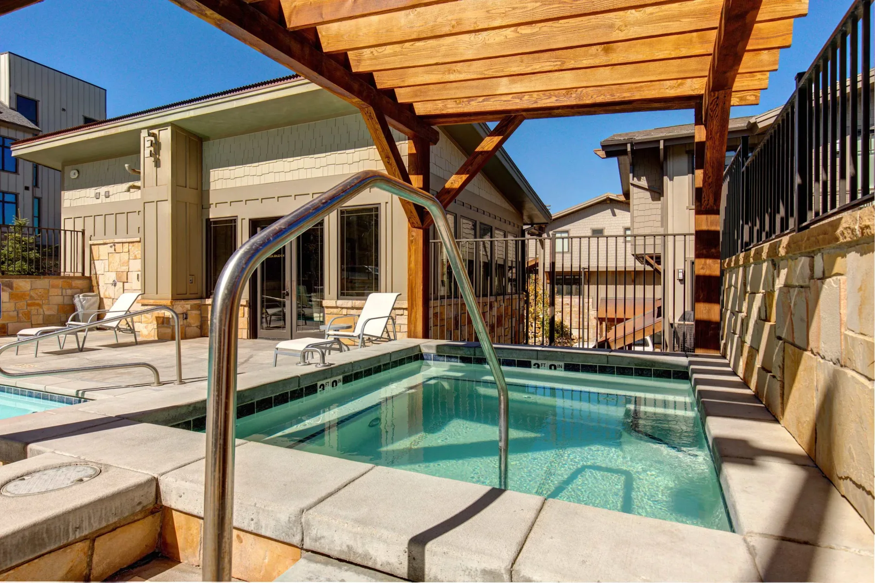 Zona común: Una piscina exterior está bajo una pérgola de madera junto a un edificio.