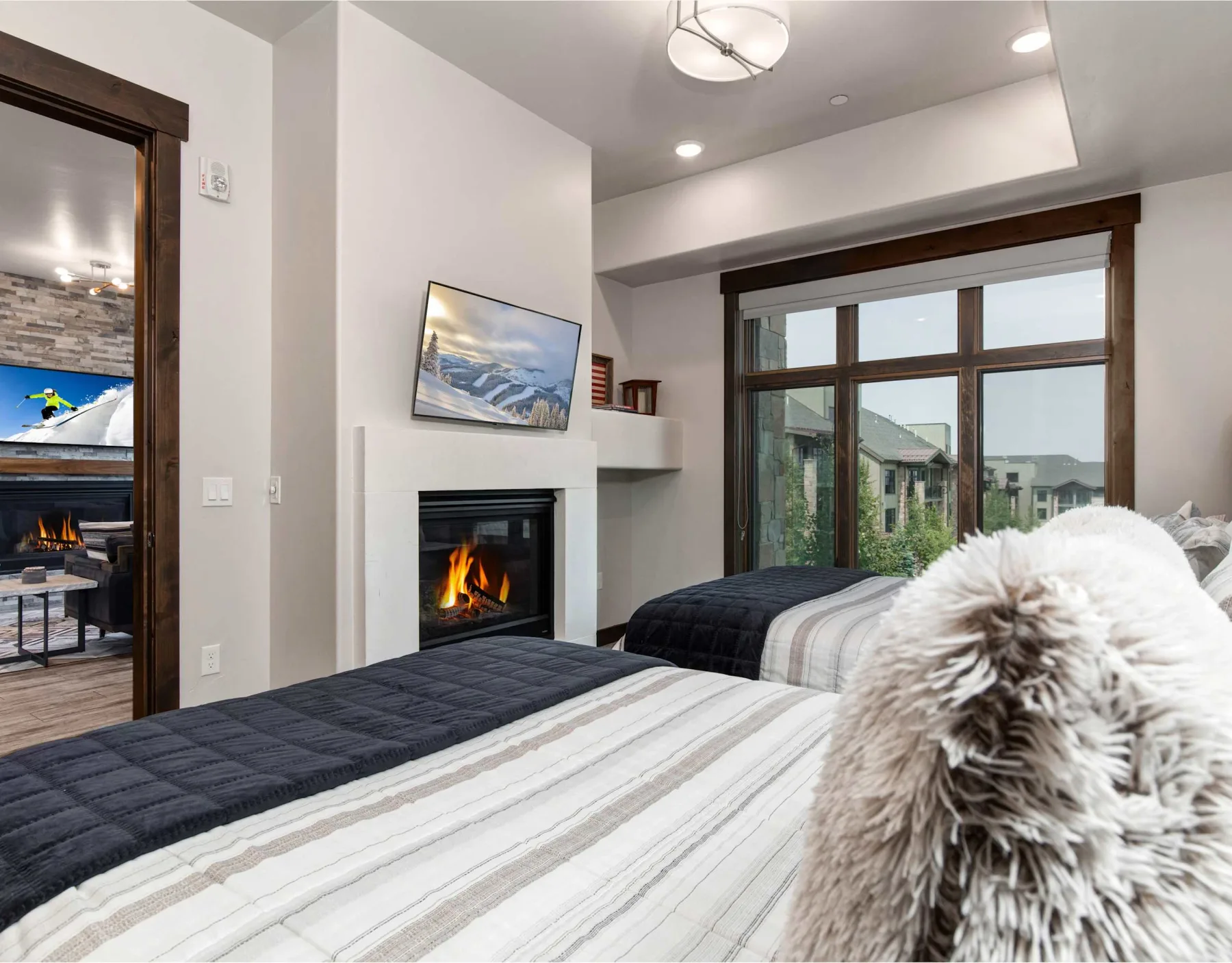 Un dormitorio con camas, una chimenea y una ventana grande con edificios cercanos a la vista.