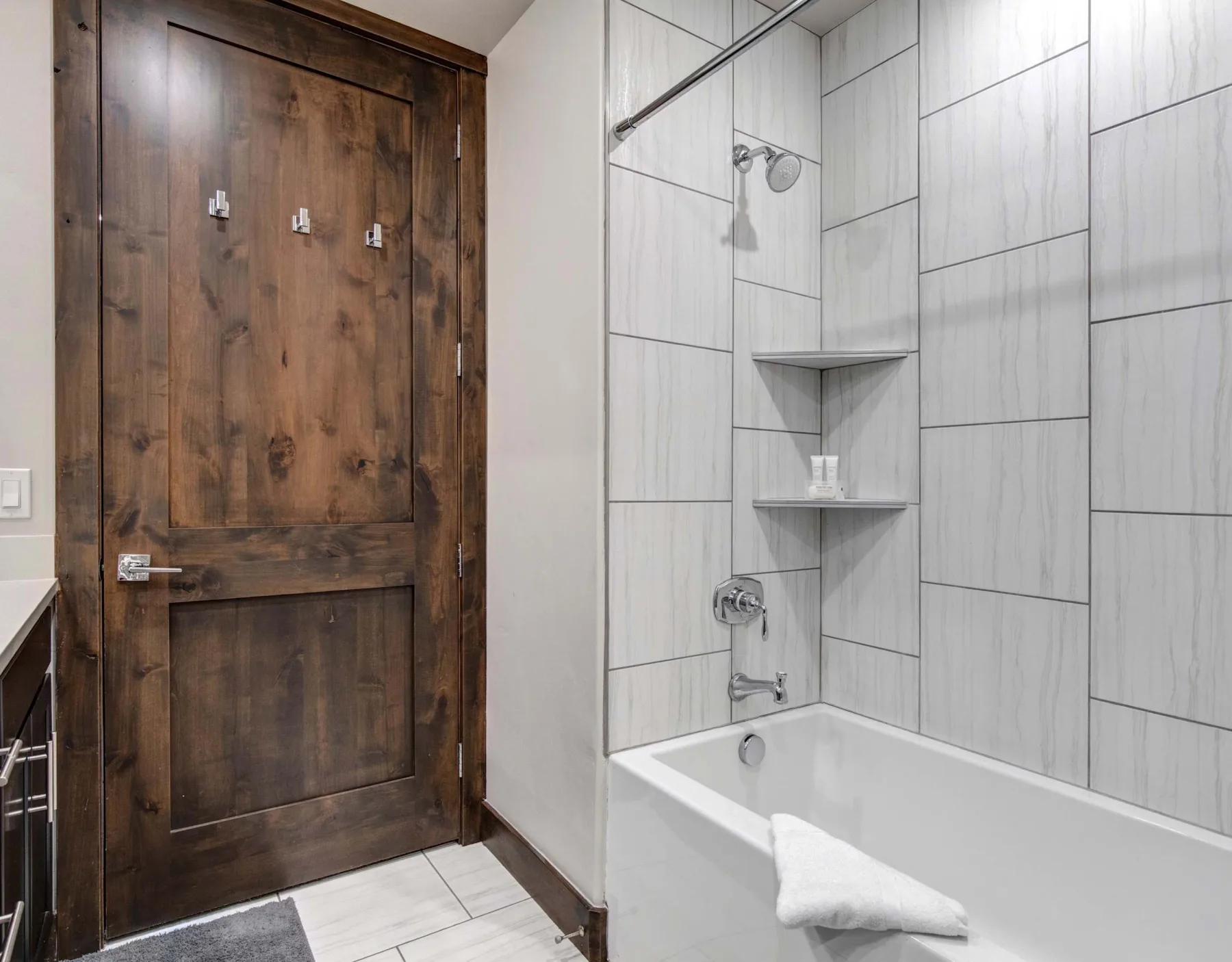 Un baño con azulejos, una bañera y una puerta de madera oscura.