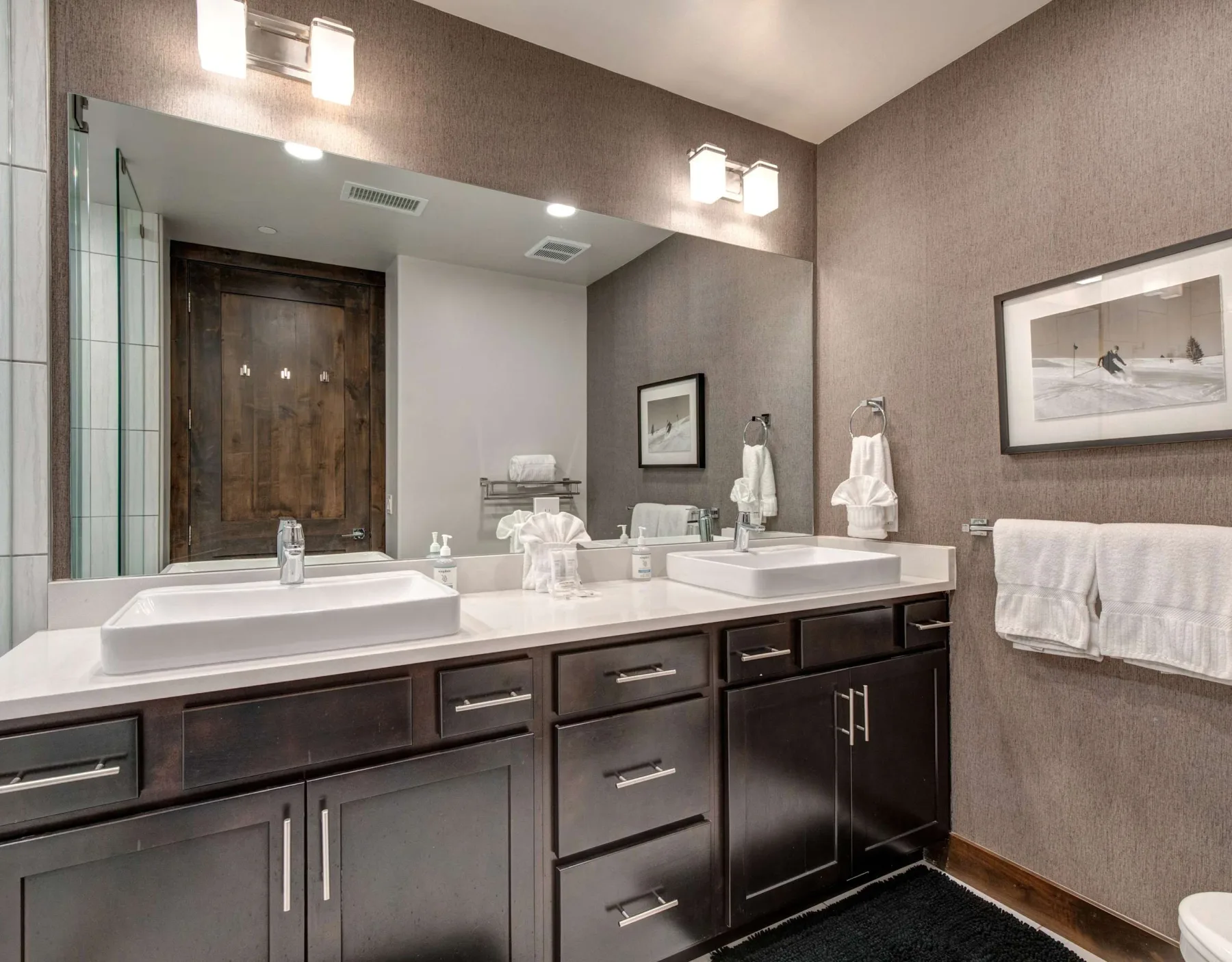 Un mueble de baño con dos lavabos está bajo un espejo amplio.