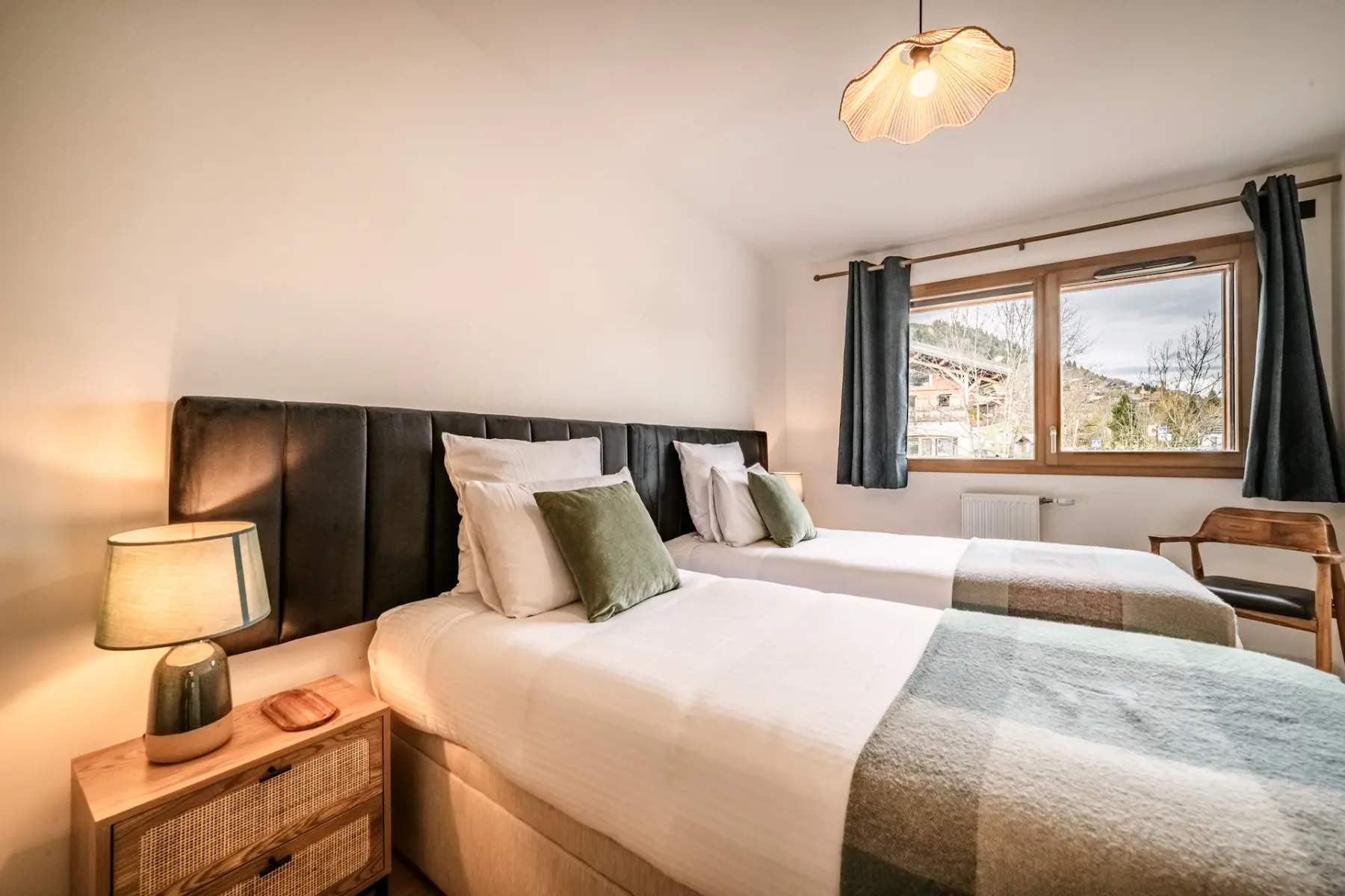 Un dormitorio con dos camas, luz junto a la cama y una ventana al exterior.